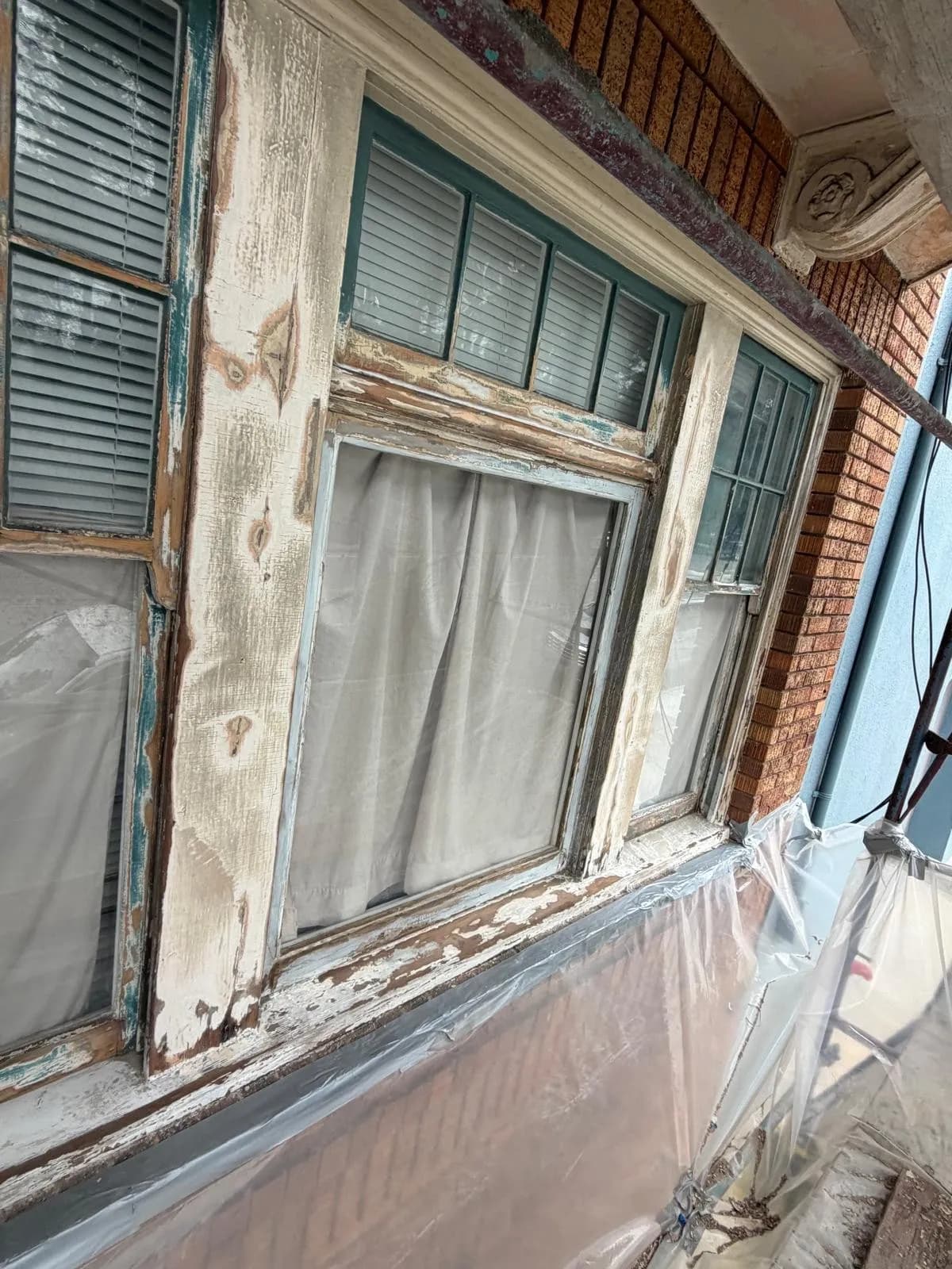 Window frame with peeling paint scraped back to wood, and plastic sheeting below the sill