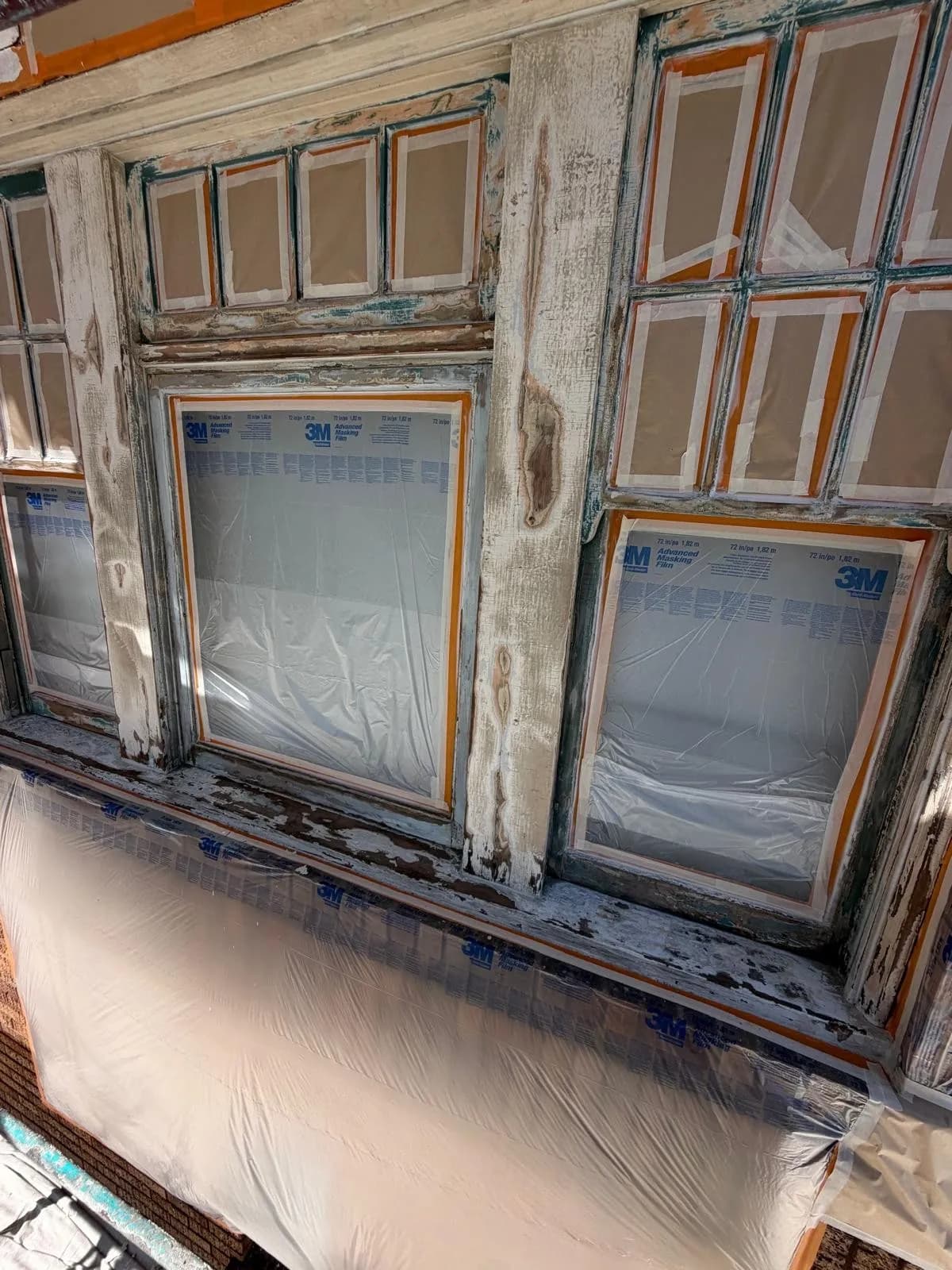 Bay windows masked with film and tape, wood mullions scraped bare