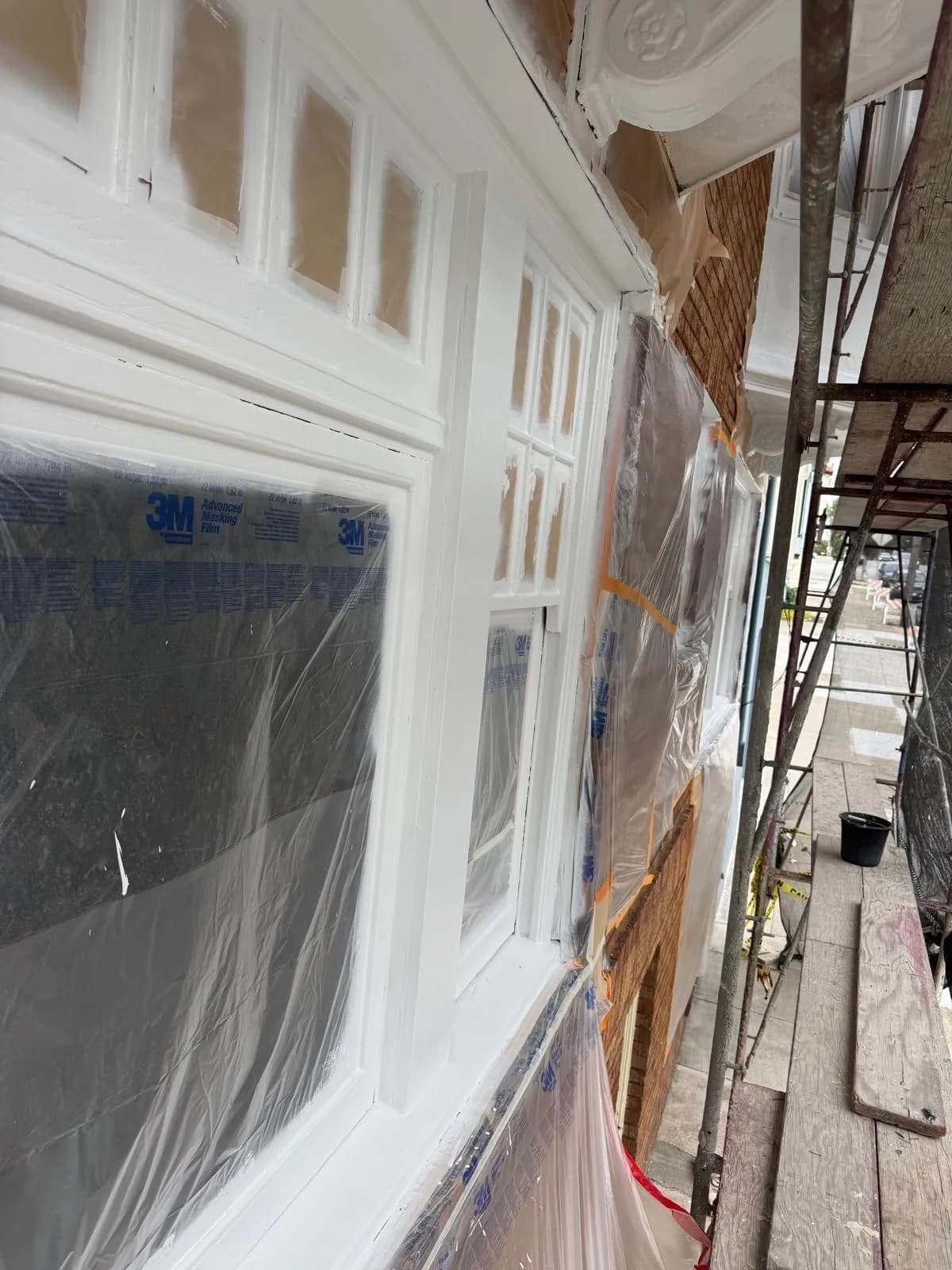 White window trim with masking film still on the glass, and scaffolding along the bay