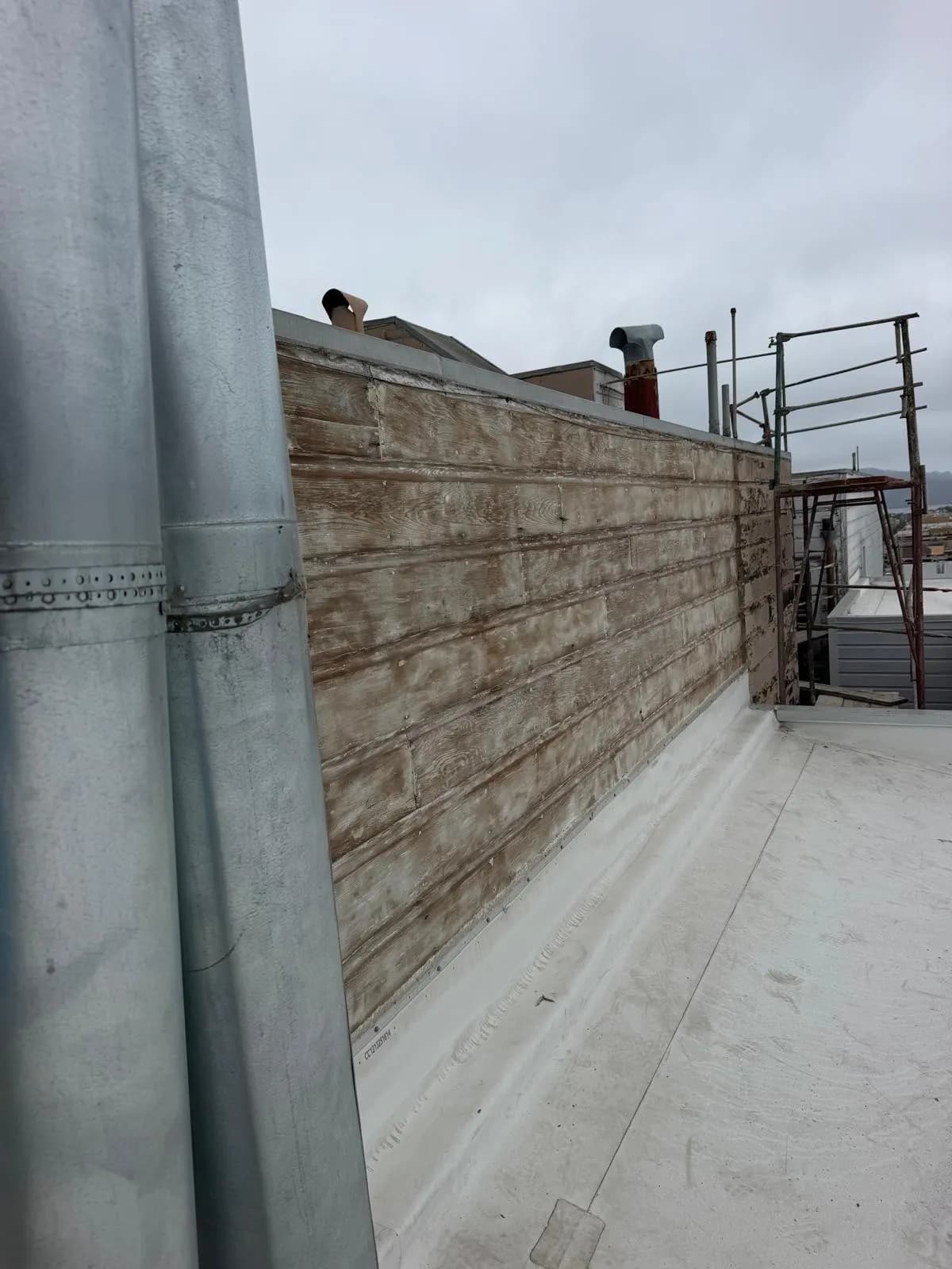 Weathered horizontal wood boards on a roof parapet, with a metal pipe in the foreground