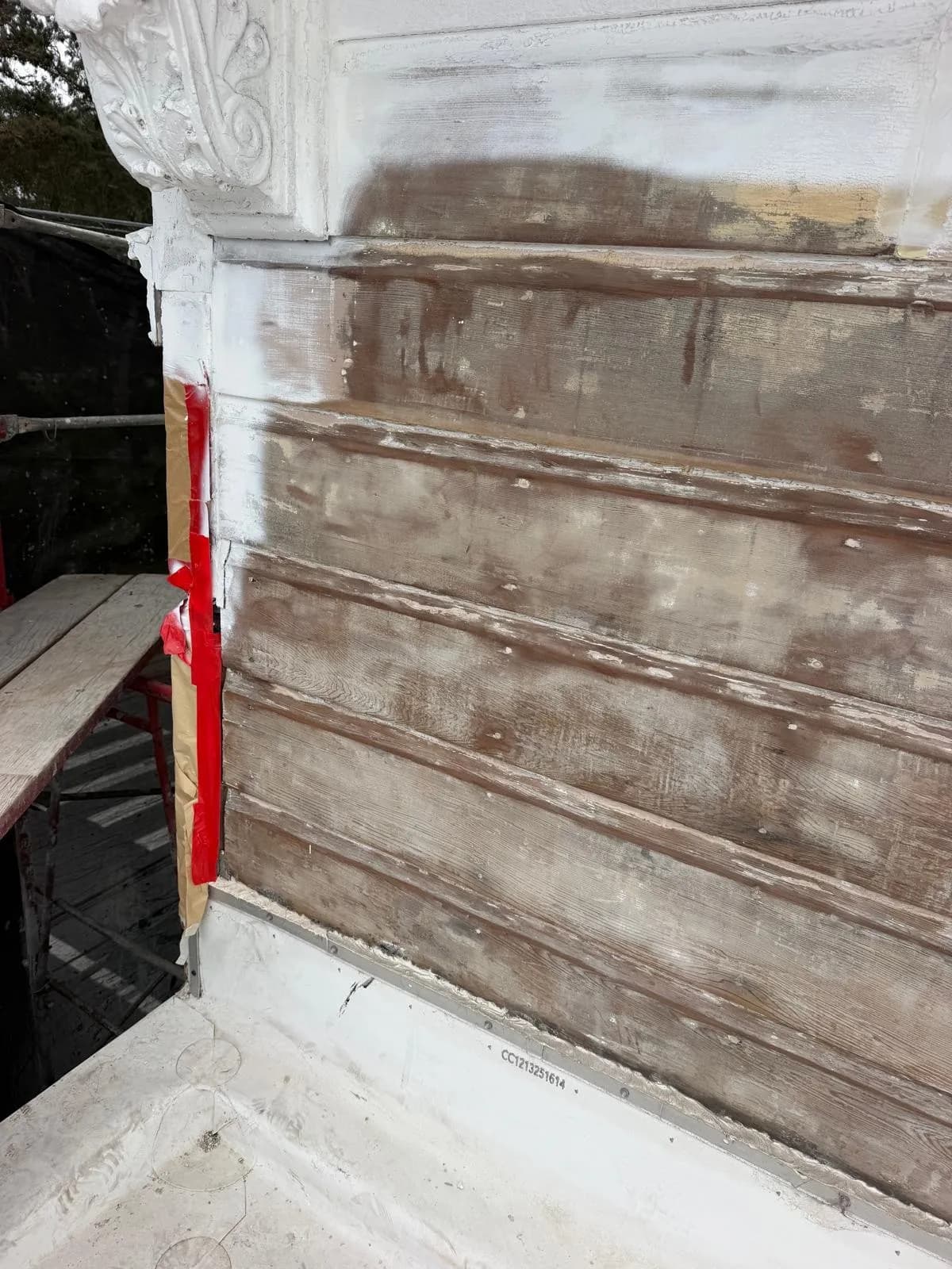 Parapet corner with a white-coated bracket beside wood boards that are still bare and weathered
