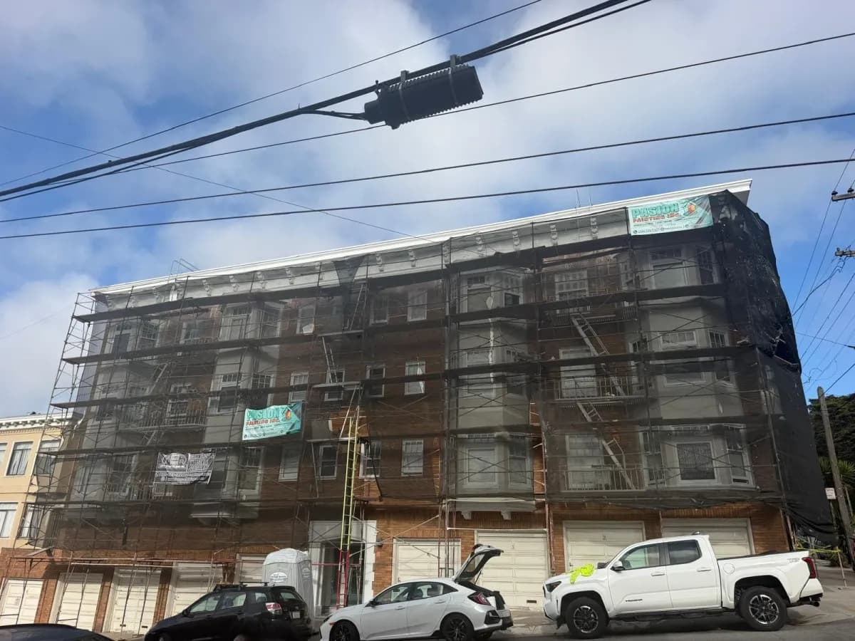 Full street facade of the brick apartment building inside scaffolding and dark protective mesh