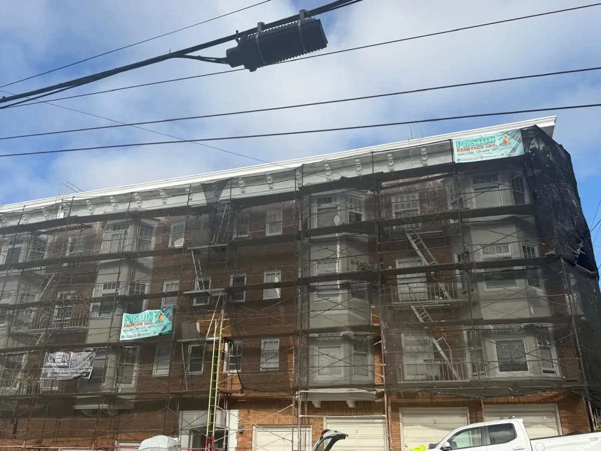 Closer view of the same brick building under scaffold, with bay windows and fire escapes behind the mesh