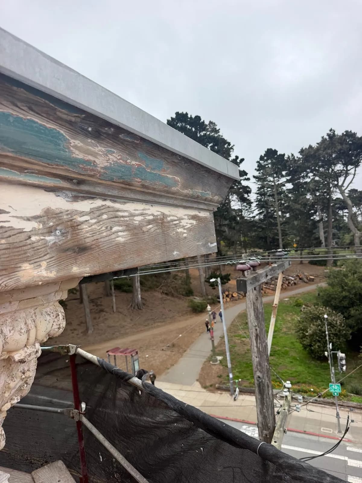 Wood cornice with peeling white and teal paint, seen from the scaffold
