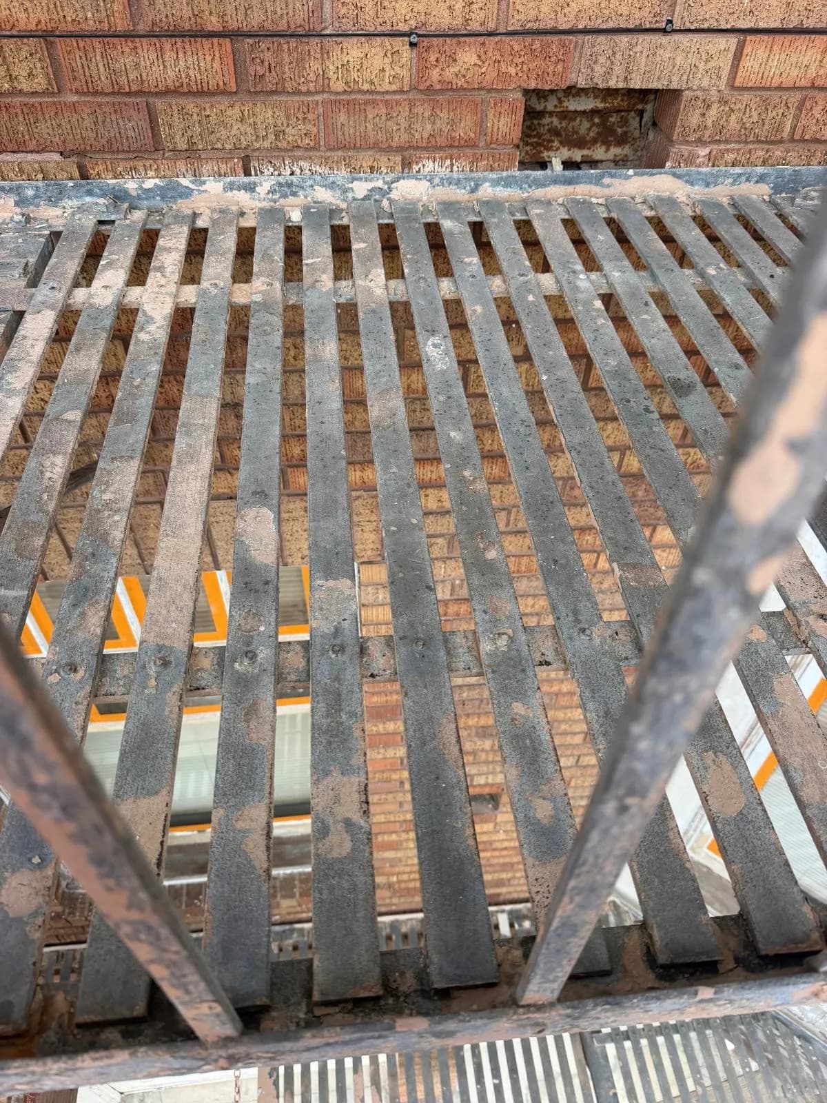Rusty metal grate with flaking paint, above a window and below a brick course