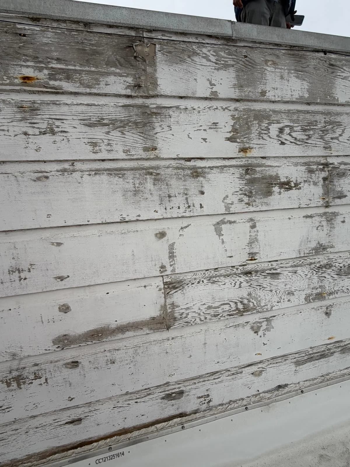 Close view of weathered white paint worn through to the wood grain on a parapet