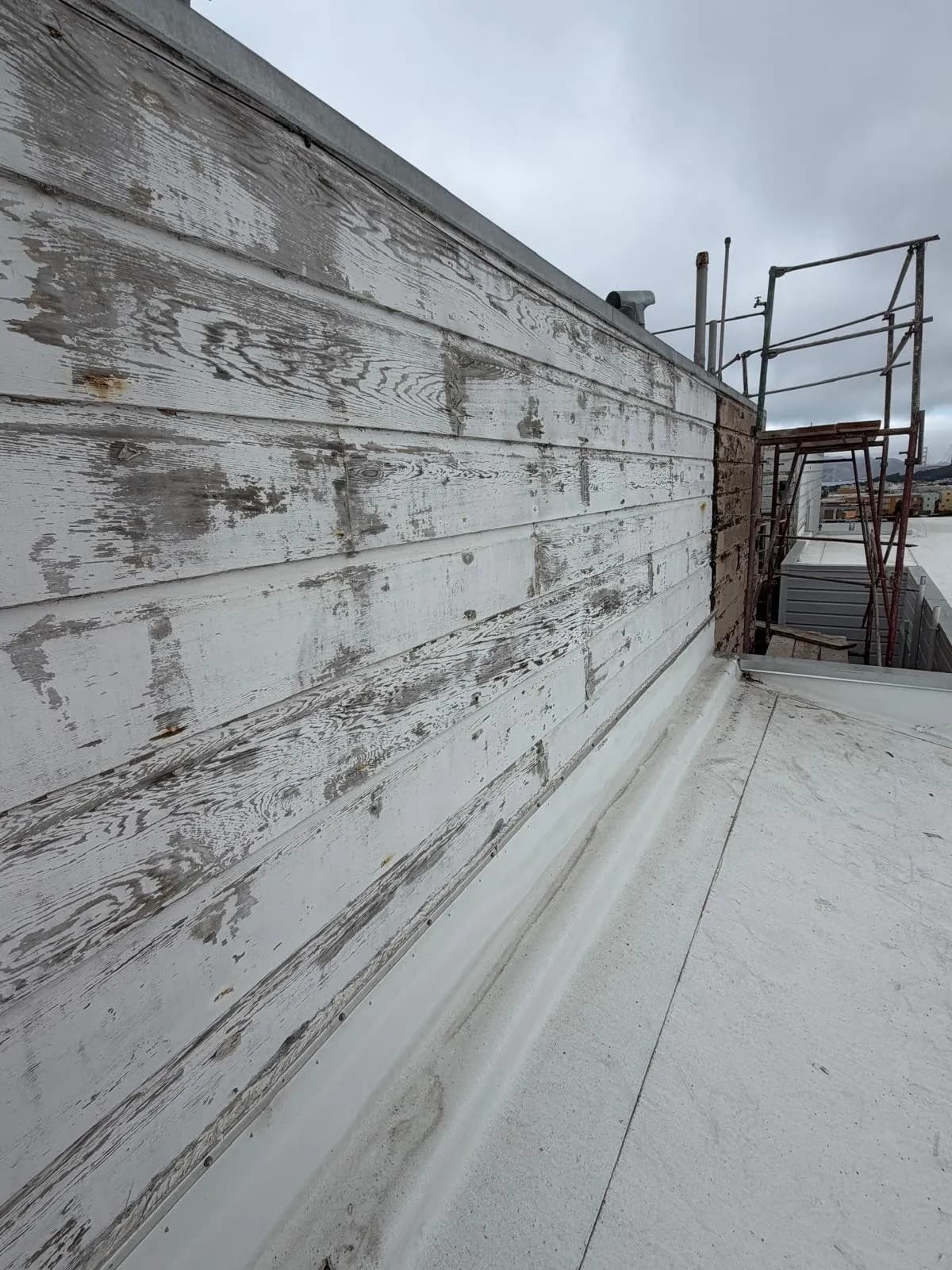 Long run of peeling parapet siding along a flat roof, with scaffolding at the far end