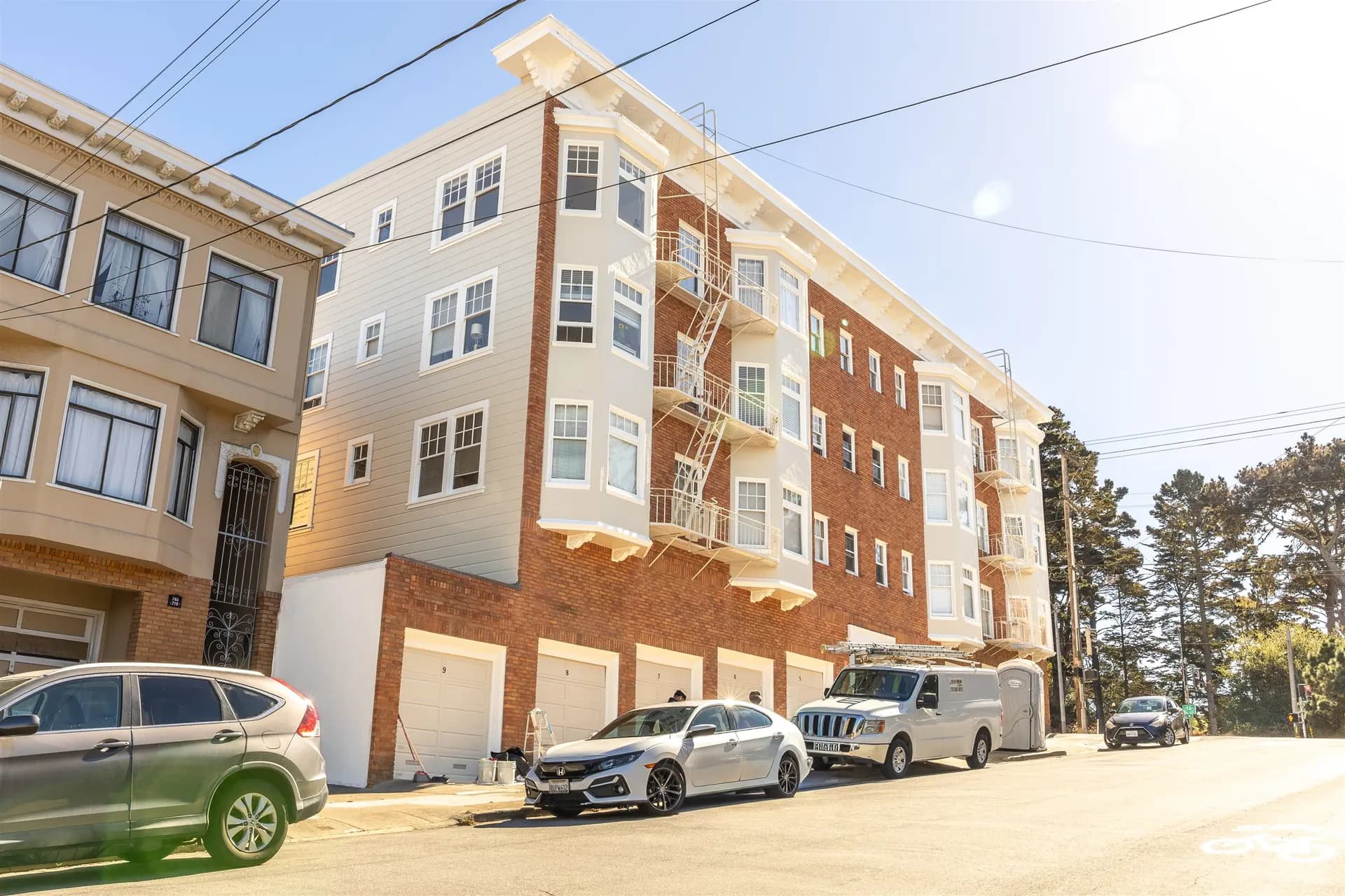 Angled view of the finished brick apartment building in San Francisco with white bays, cornice, and a row of white garage doors