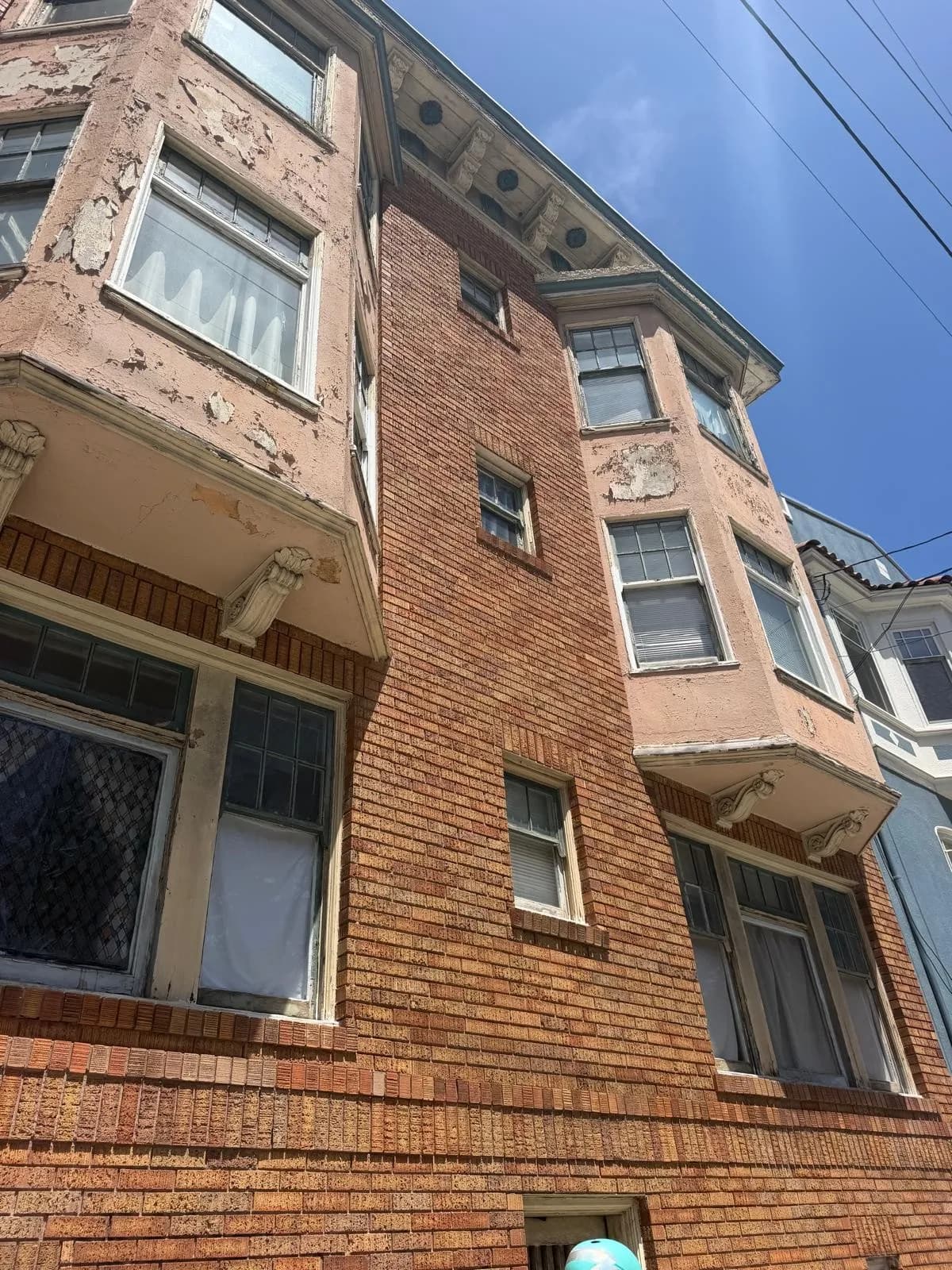 Brick facade and bay windows with peeling paint on the bay walls and window trim