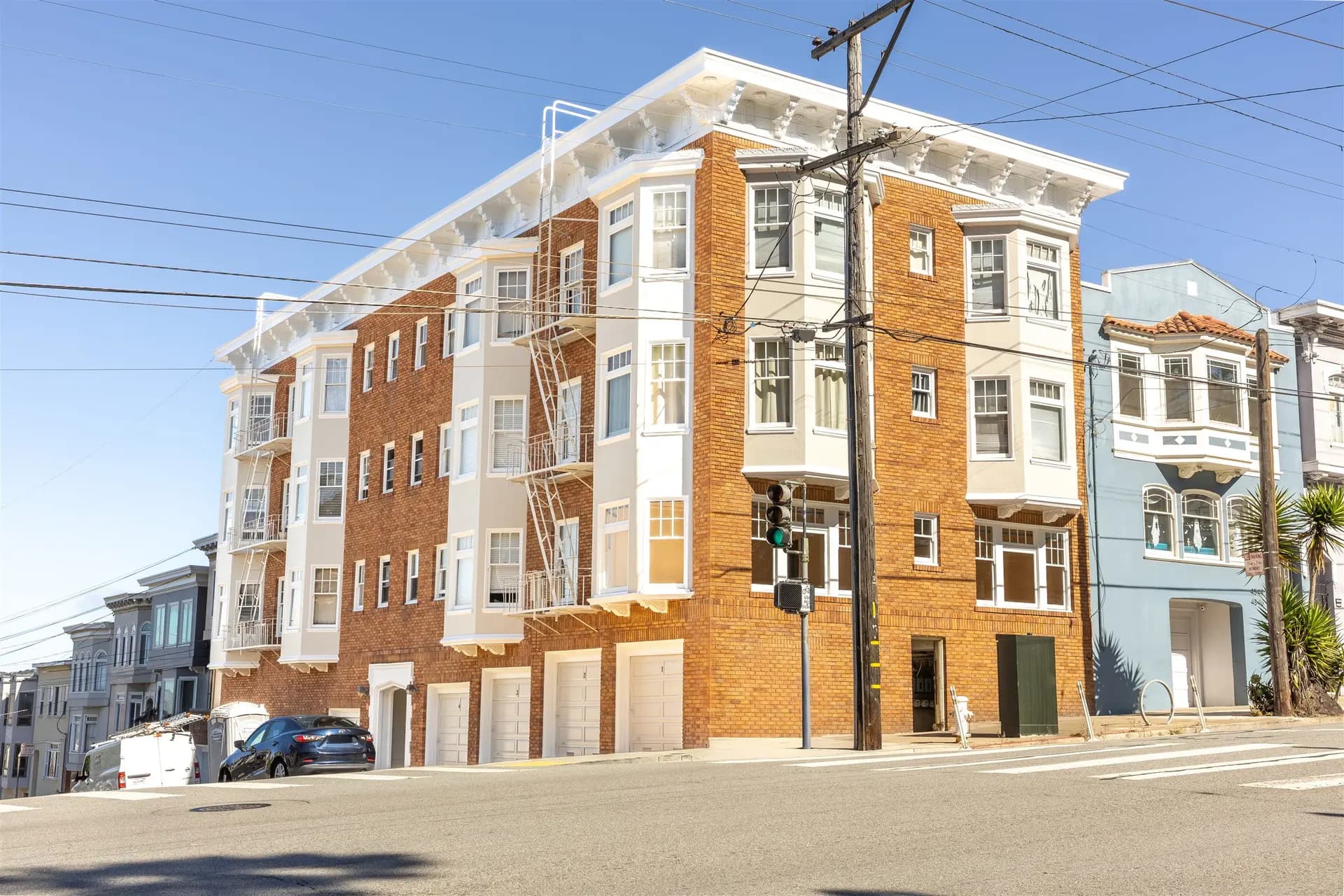 Exterior repaint of a 4-story brick apartment building in San Francisco with white trim, bay windows, and garage doors by Pasion Painting
