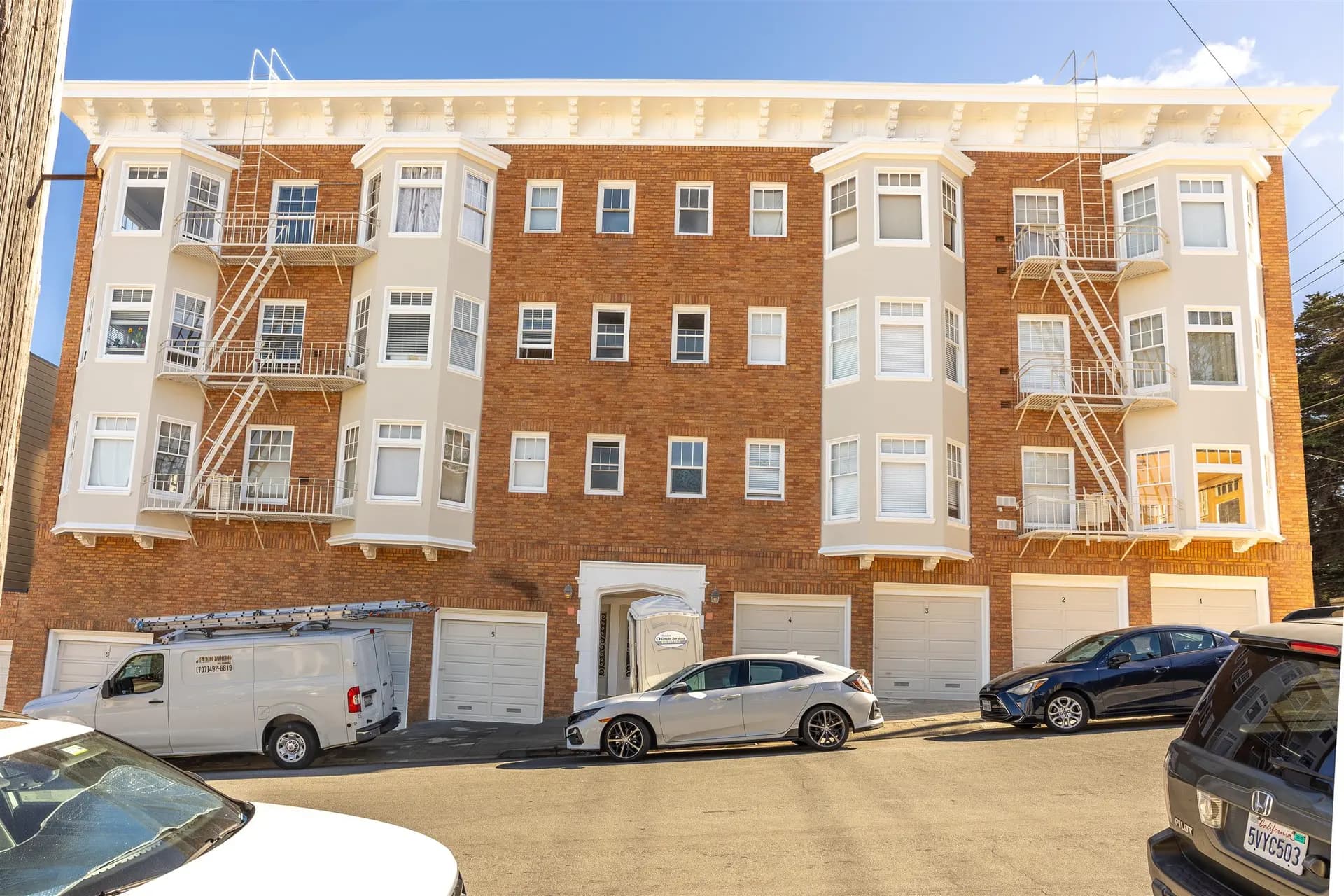 Finished street facade of the 4-story brick apartment building with white bay windows, cornice, fire escapes, and garage doors